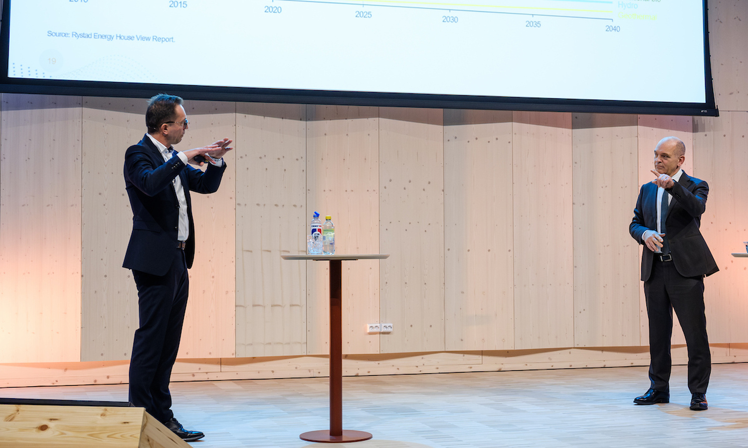 To menn i mørke dresser og hvit skjorte snakker sammen og gestikulerer med armene